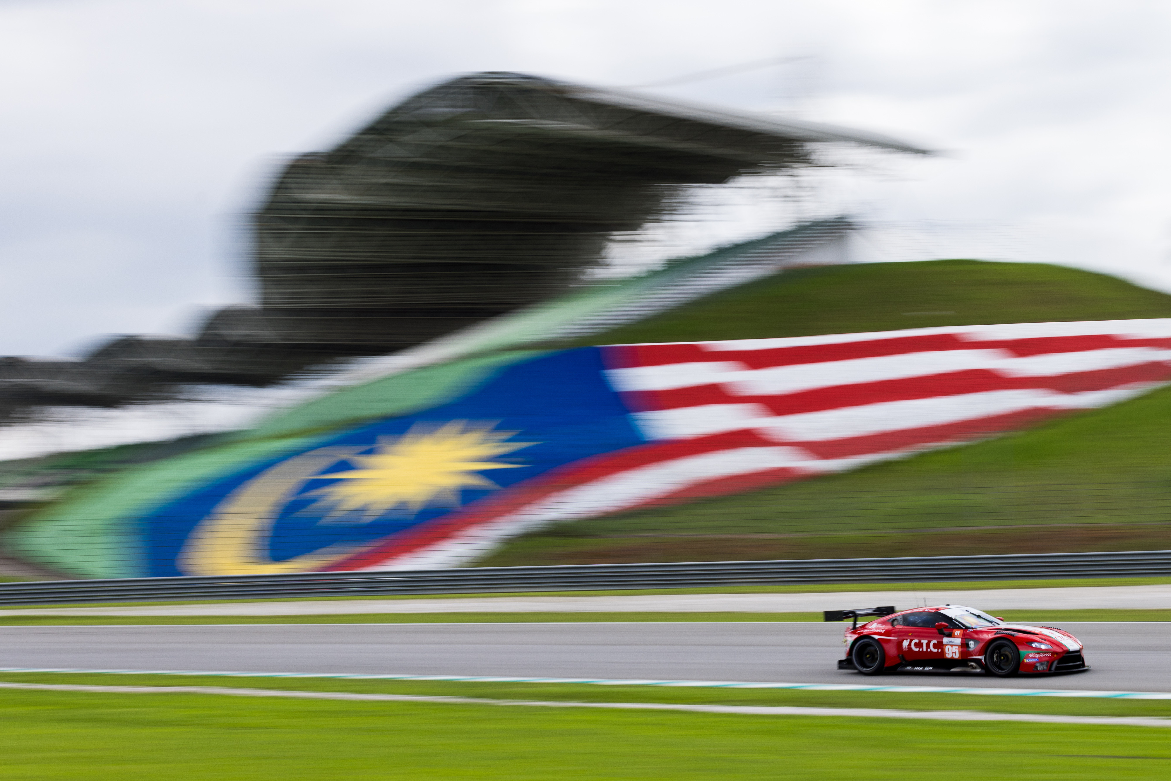 Aston Martin race car racing past the Malaysian flag at the sepang race circuit